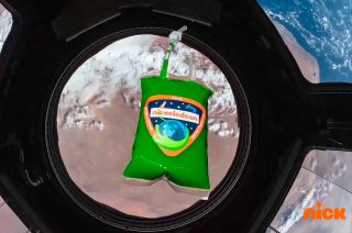 A bag of Nickelodeon green slime floats above Earth inside the Cupola aboard the International Space Station.