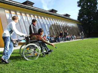 Other students watch as boy in wheelchair plays lawn game. 