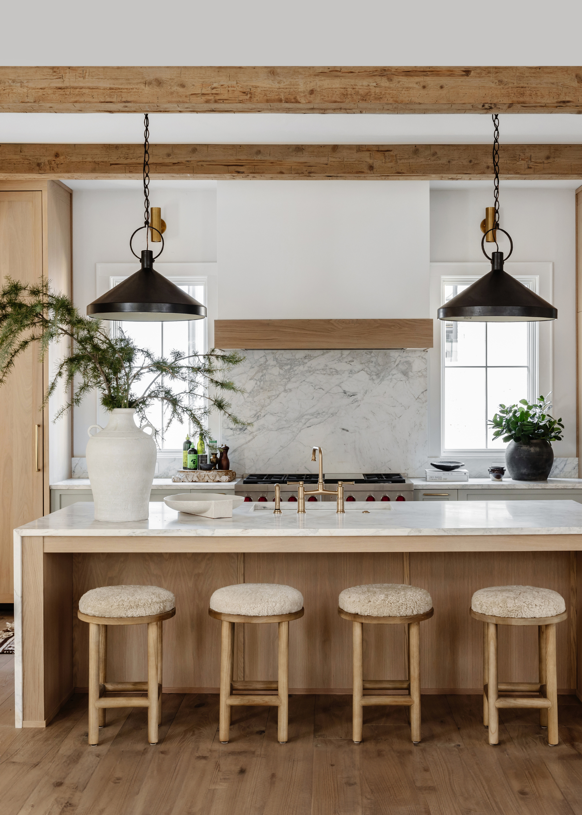 A white kitchen with lots of wood, exposed beams, wooden floor, wooden cabinetry and four bar stools sat neatly underneath the wood island