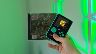 Phil Hayton holding Super Pocket and Legacy of Kain Soul Reaver for PS1 in one hand in front of green lighting