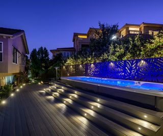decked backyard space with pool and hot tub lit up at night