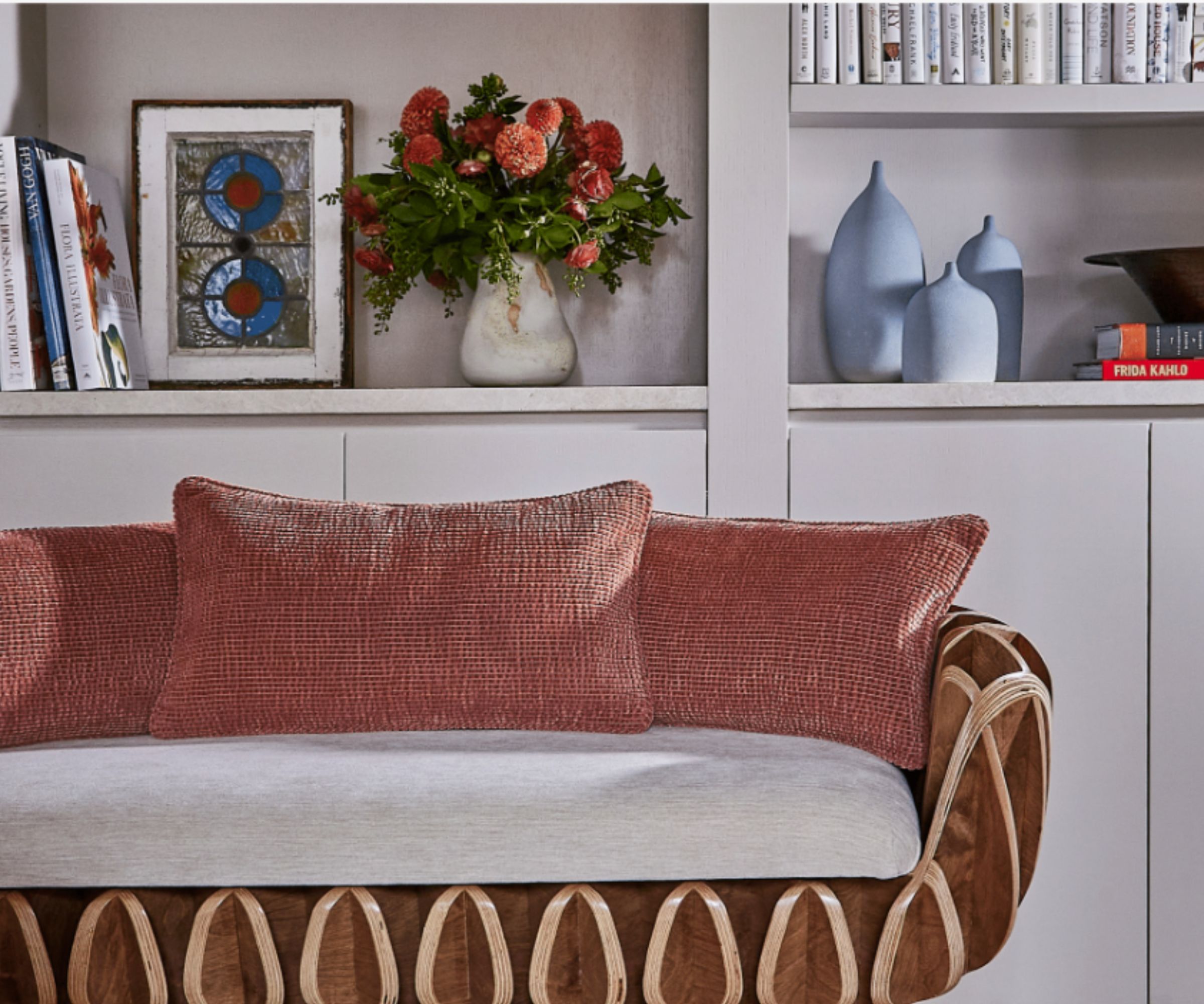 Curved sofa with wooden frame and upholstered cushions, white shelving behind decorated with vases and books
