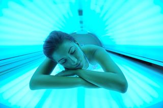A young woman lies in a tanning bed.