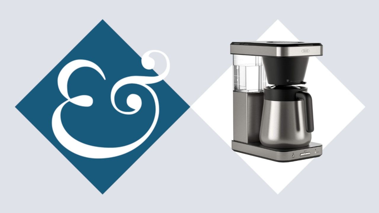 A stainless steel drip coffee maker on beside a blue diamond with an &amp; sign in it. 