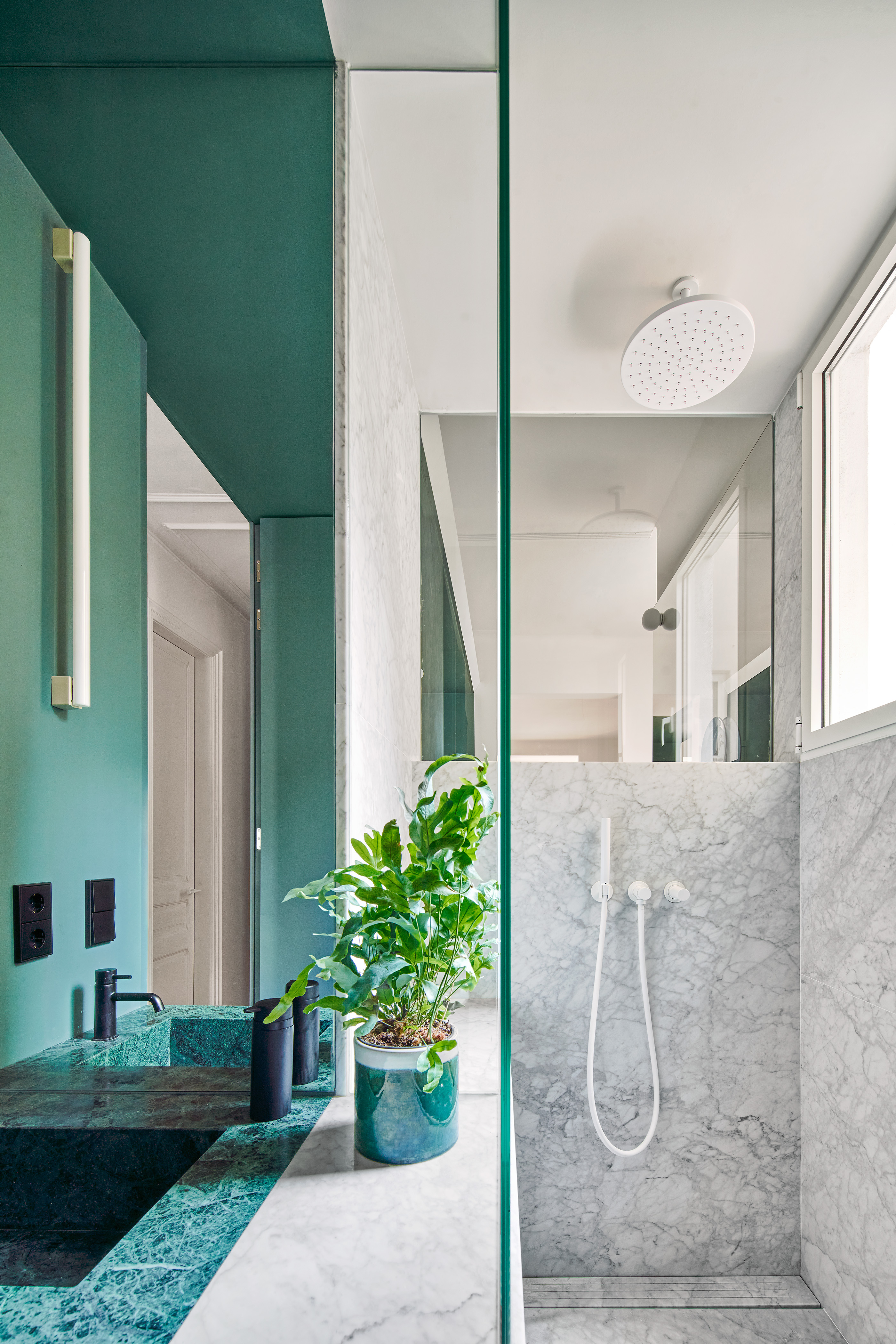 A small bathroom painted a deep green tone, with the shower in natural stone color