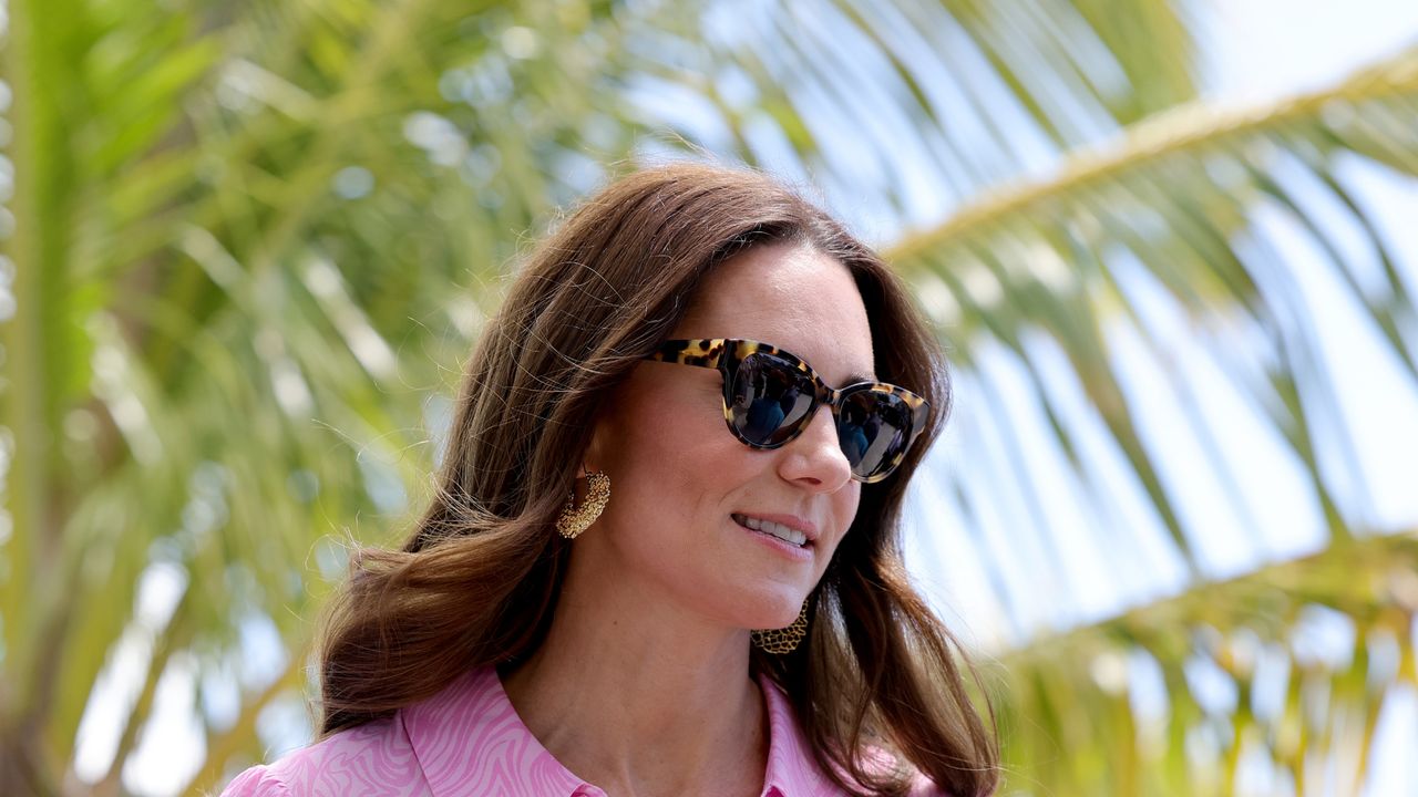 Kate Middleton wearing tortoise print sunglasses and a pink dress standing in front of a palm tree