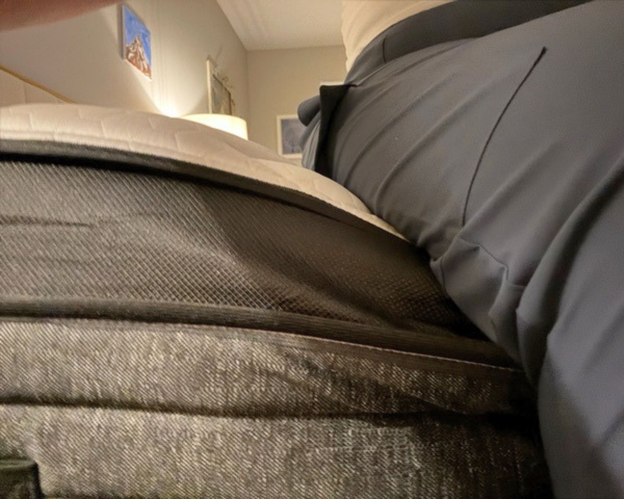 Someone sitting on the side of the Nolah Evolution mattress, wearing dark grey trousers, to test the edge support.