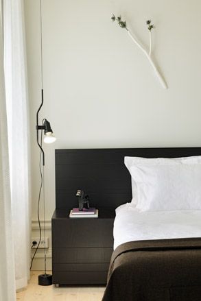 A square-on view of a bed with white linen, a brown throw, a side and head board with books on top and a lamp standing above from the floor.