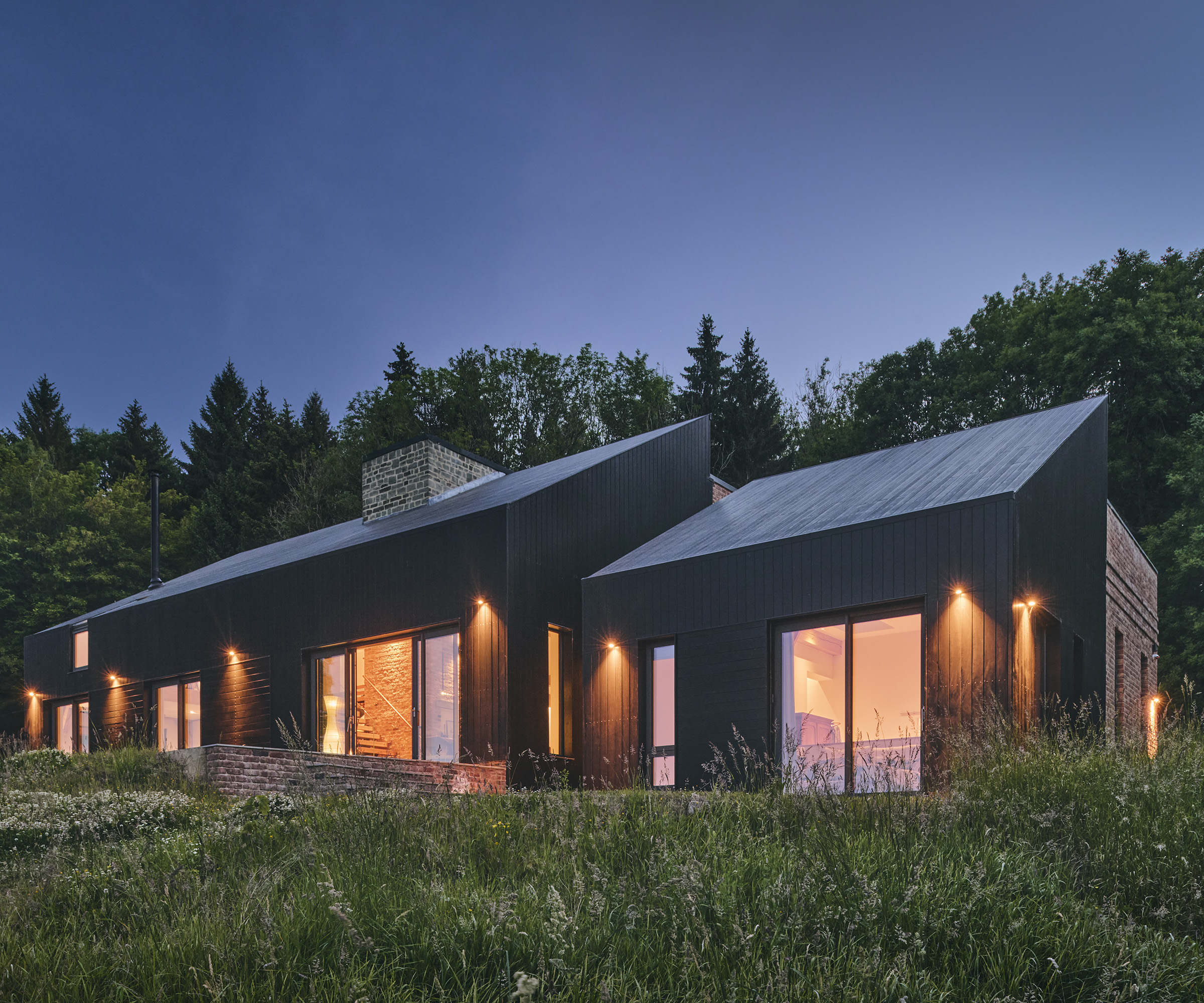 Exterior of a contemporary barn-style self build clad in black zinc and lit up at dusk
