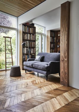 A living room with grey sofa and a wooden chevron panelled floor