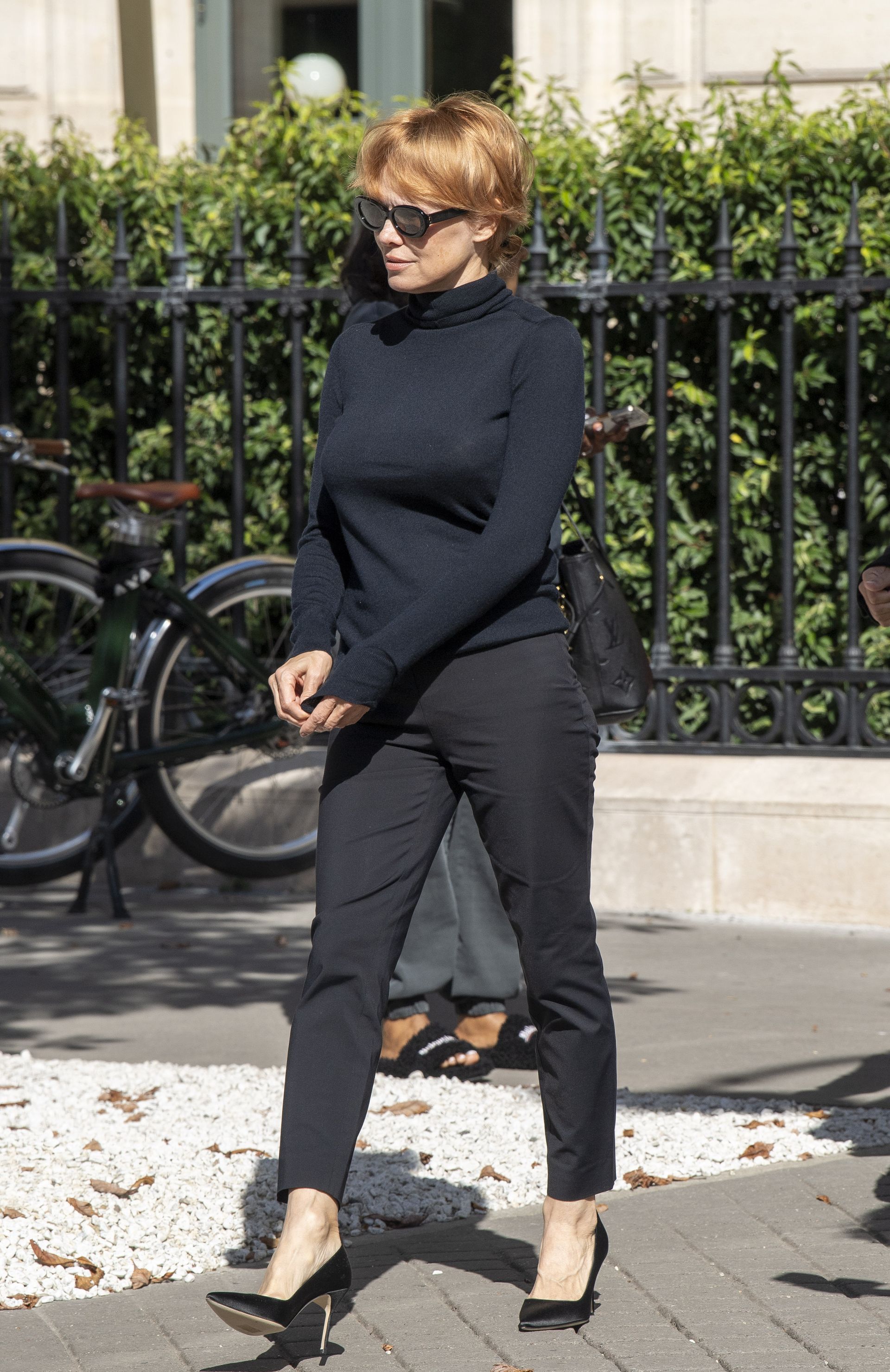 Pamela Anderson wearing a black turtleneck, black cigarette pants, and black pumps