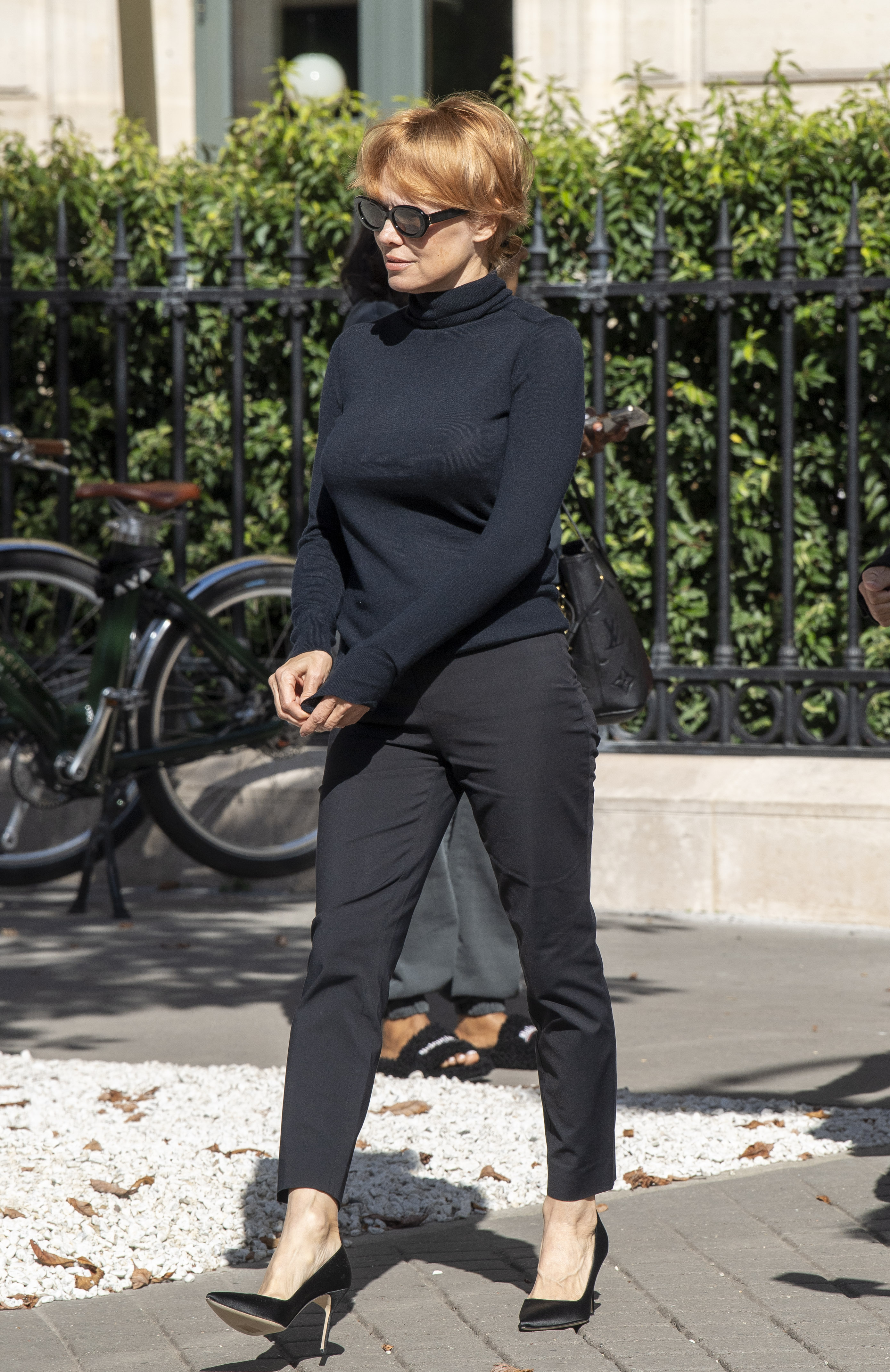 Pamela Anderson wearing a black turtleneck, black cigarette pants, and black pumps