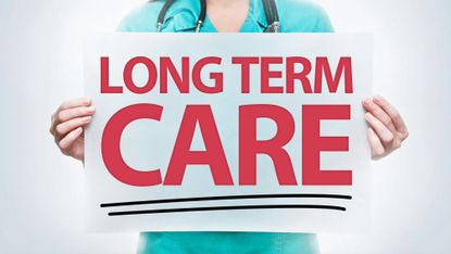 Close up of a health worker in scrubs holding up a sign reading Long Term Care