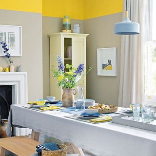 A dining room with cream storage, neutral and yellow walls and blue touches
