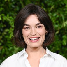 a white woman with short, dark hair posing in front of a grass background