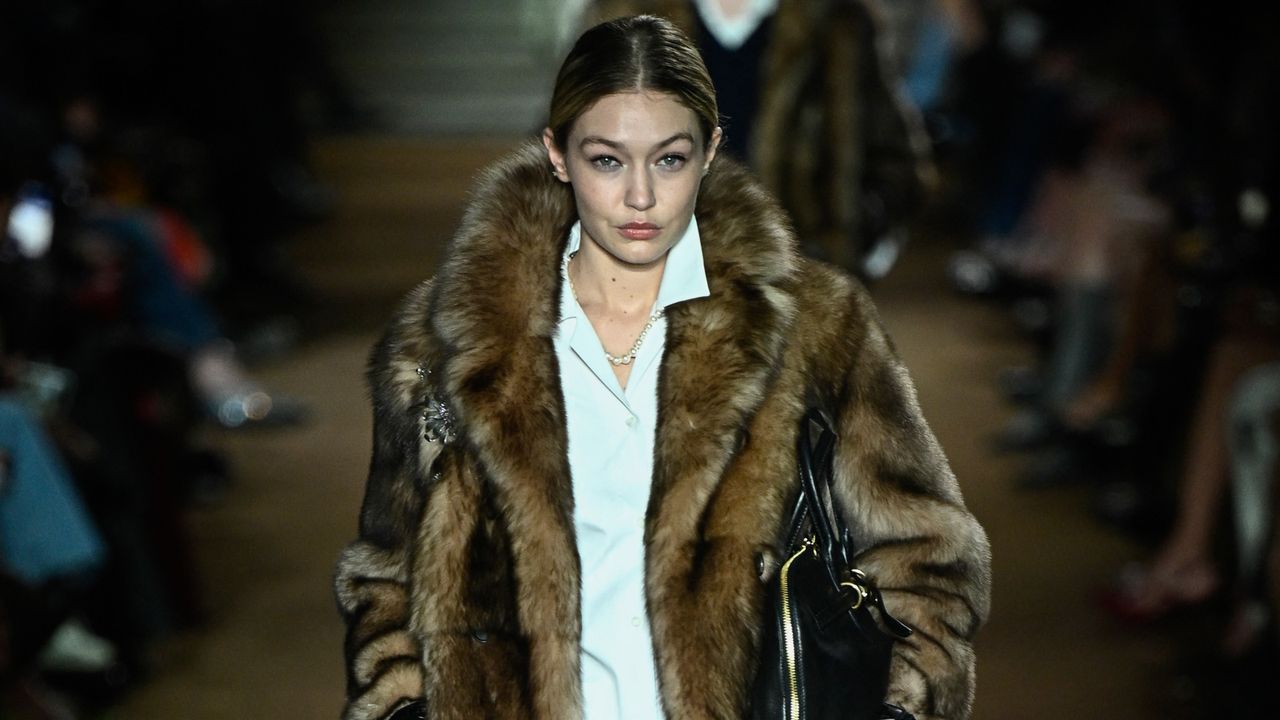 Gigi Hadid wearing a faux fur coat with a white button down dress while walking Miu Miu&#039;s show