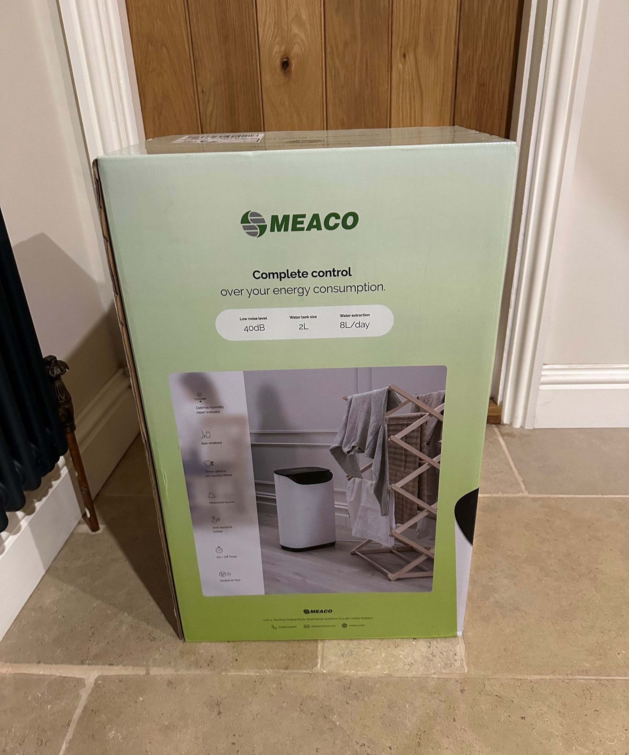 A dehumidifier in a green box on a stone floor with a wooden door behind it