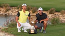Haotong Li and Jady de Beer crouch down next to the 2025 Qatar Masters trophy