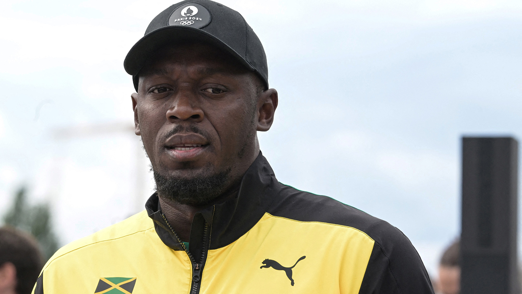 A man wearing a yellow and black jacket and a dark green baseball cap looks down