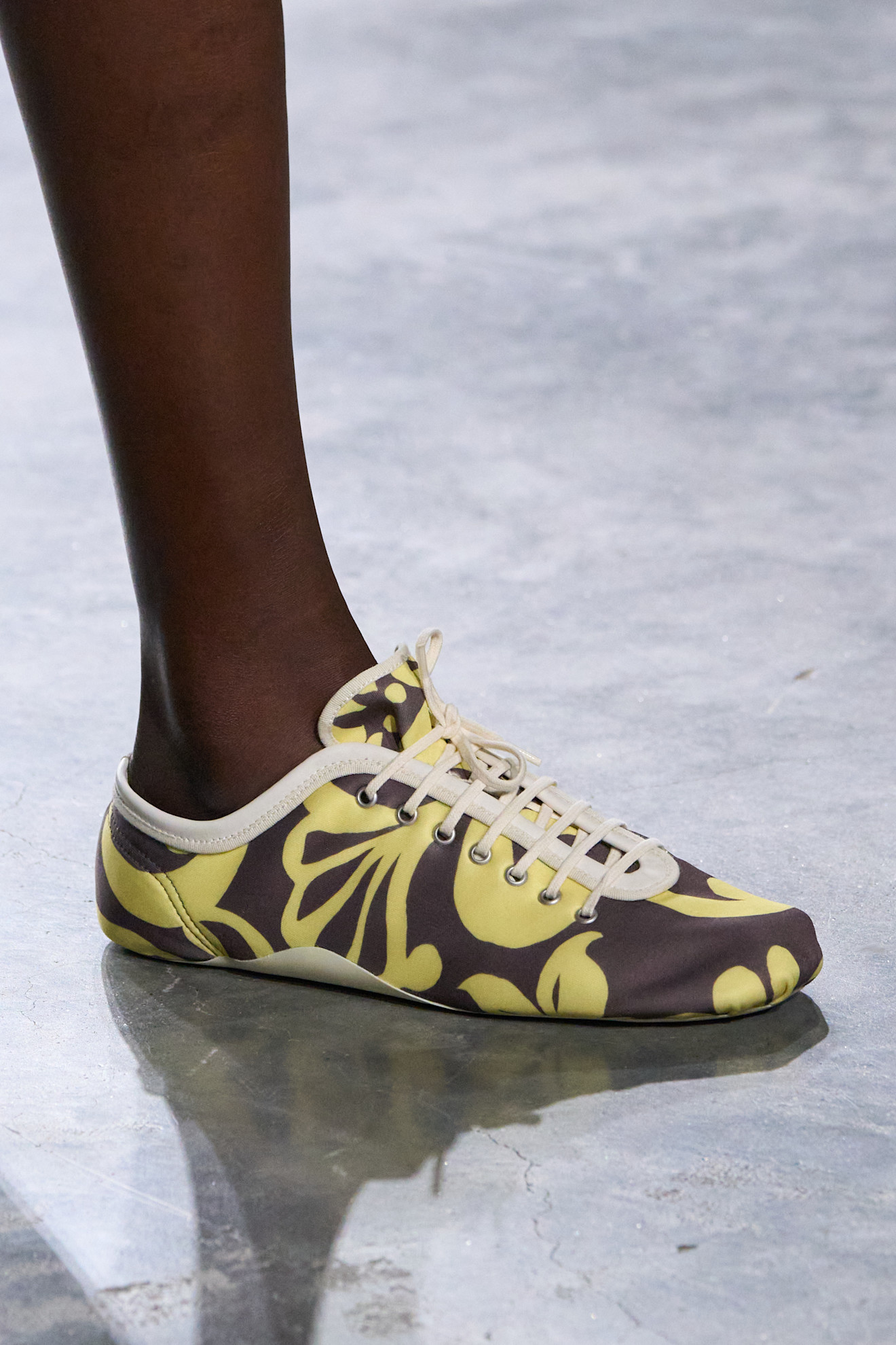 A model at the spring/summer 2026 Dries Van Noten show in Paris wearing yellow-and-brown patterned low-profile sneakers.
