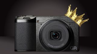 A stylish Ricoh GR IV compact camera with a gold crown on top, set against a rich black backdrop