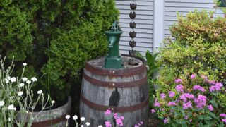 a wooden barrel turned into a water harvesting rain pot with a green water dispensing spout and a rain chain