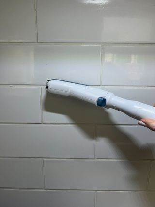 Steam cleaning grout lines on white tiles with a grout brush