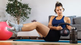 Woman performs Russian twist exercise at home using a kettlebell