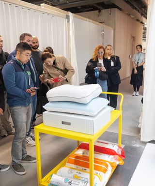 Journalists looking at a selection of IKEA's color-coded thermoregulating bedding on a yellow stand.