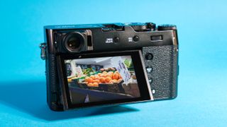 The Fujifilm X100VI mirrorless rear with the screen out against a blue background.