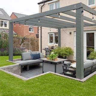 sunken garden area with paving covered with a pergola draped with outdoor lights