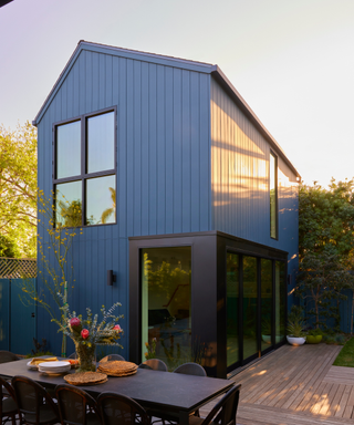 Blue painted siding on modern home with sloped roof and dining table and chairs outdoors