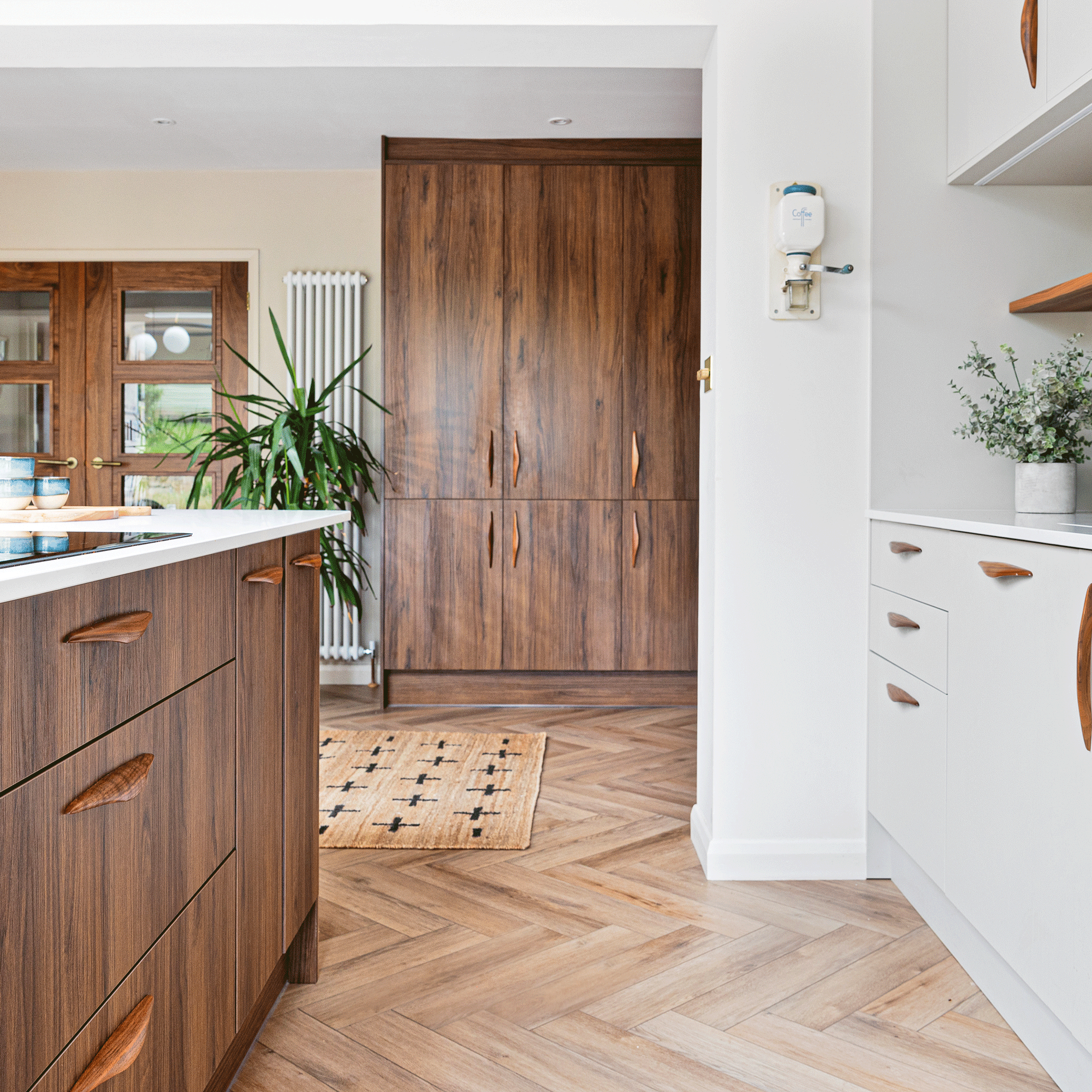 a kitchen with both dark wood and wgite cabinetry, herringbone flooring white walls and white countertops