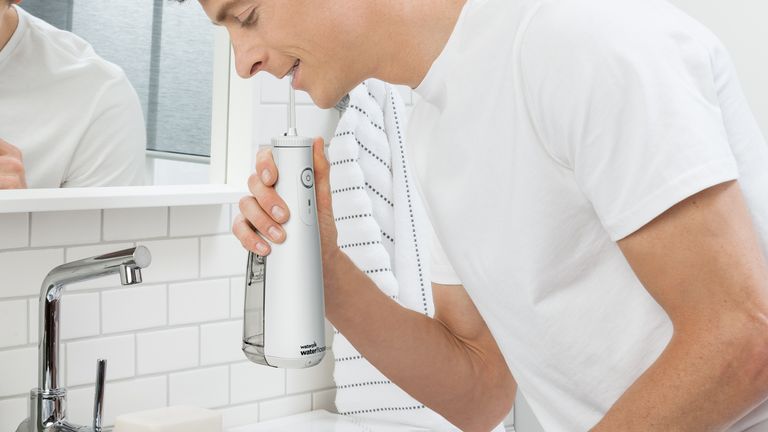 A man leaning over a sink using the Waterpik cordless model, one of the best water flossers you can buy.