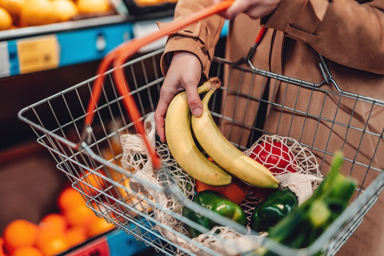 Young woman holding shopping basket filled with fruit and vegetables in supermarket.