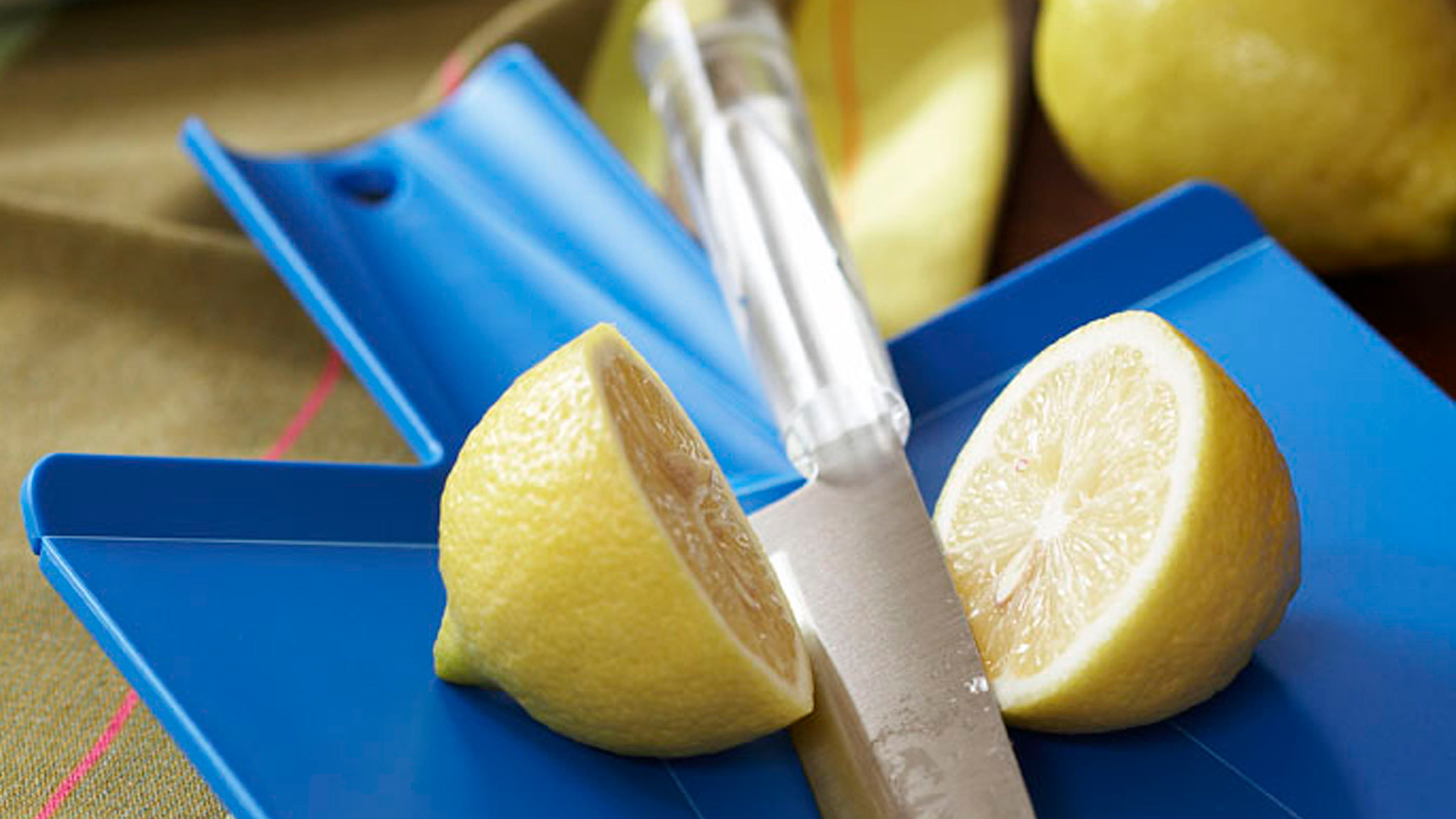 A lemon being cut with a stainless steel knife on a blue plastic cutting board