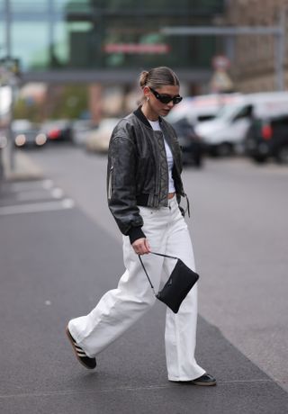 woman wearing leather jacket, t-shirt, white pants, and adidas sambas