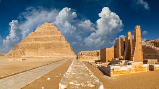 We see the step pyramid against a blue sky with clouds.