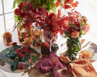 Thanksgiving centerpiece ideas with warm-colored seasonal florals in a white vase, with orange, red and green tableware