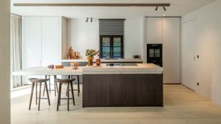 split level kitchen island in cream and dark wood kitchen with seating area at one end and cooking/prep area at other