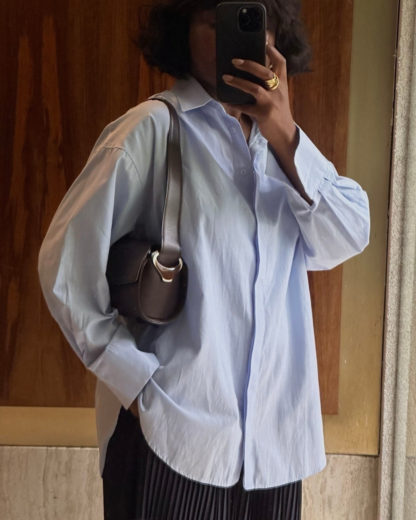 French influencer @frannfyne takes a mirror selfie wearing a button-down shirt with a brown leather bag.