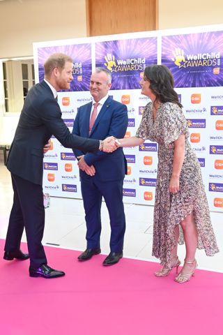 Prince Harry shaking a woman's hand on the red carpet at the Well Child Awards with a man watching on