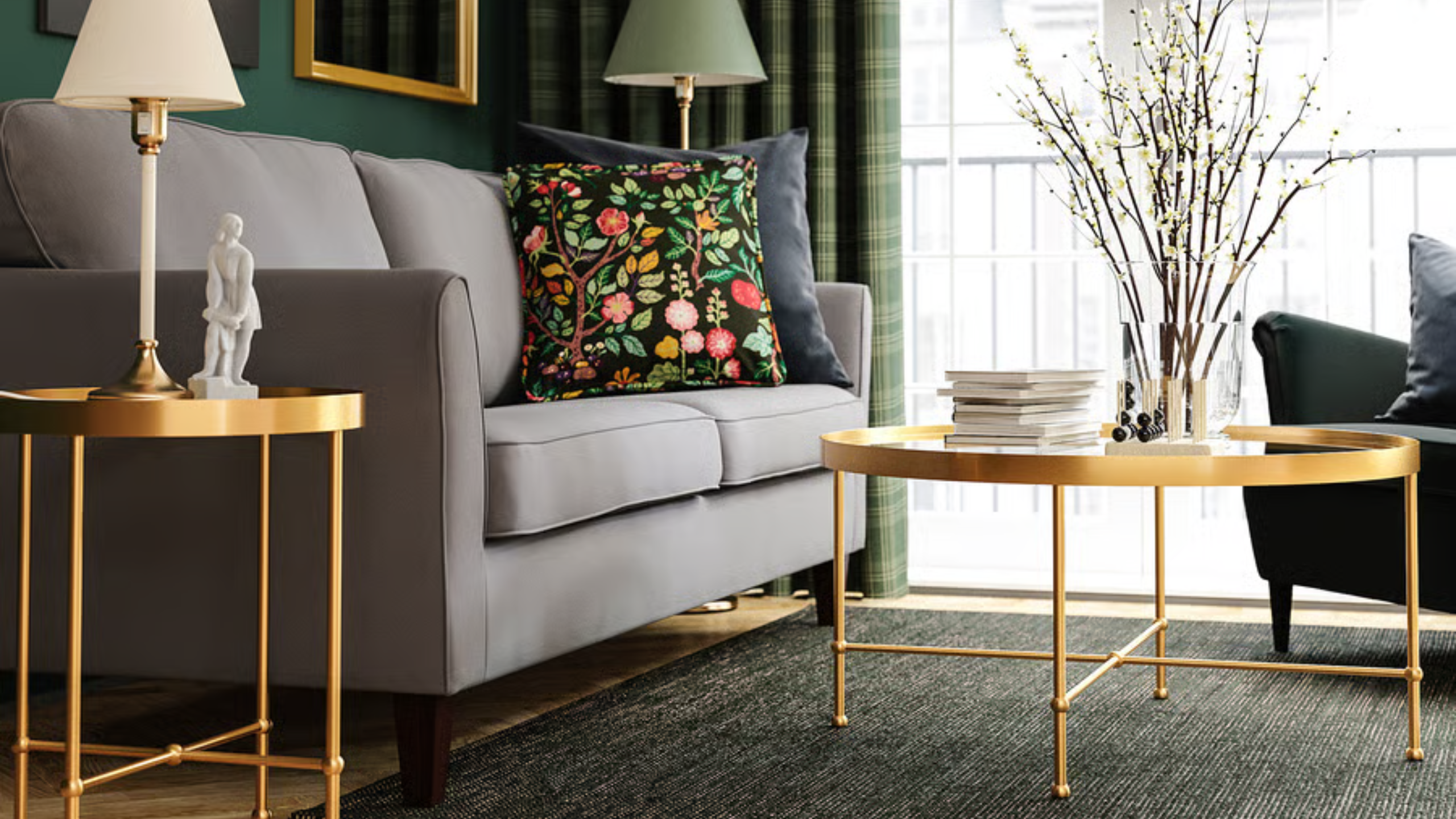 Empire-style glass IKEA coffee table with a gold frame pictured in an opulent living room alongside a coordinating side table, grey sofa, two lamps, and a large sliding glass door.