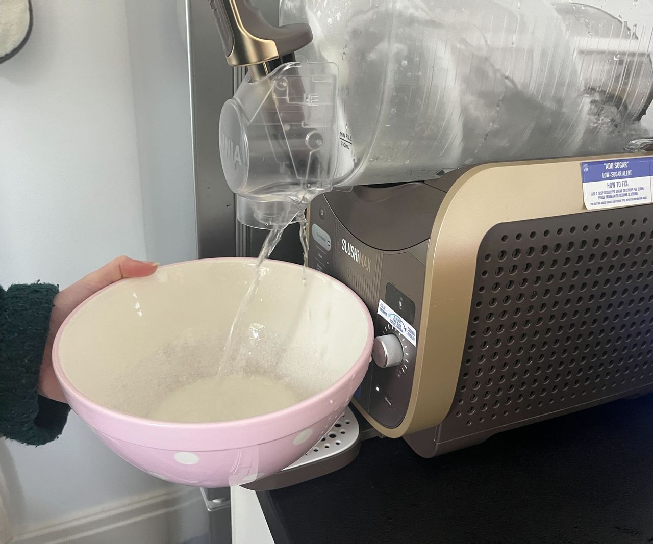 Dispensing plain water from the Ninja SLUSHi max into a pink mixing bowl.