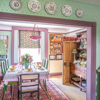 Dining room with antique furniture, green patterned wallpaper, pink painted woodwork and vintage chinaware