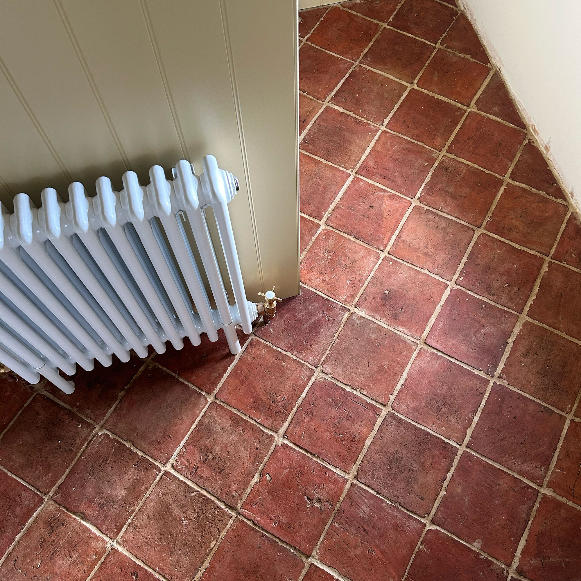 Above view of terracotta tiles on floor in room with panelled walls and white radiator