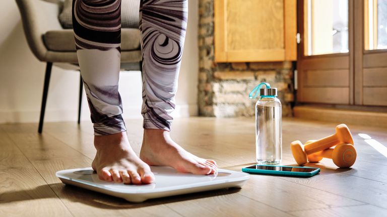 How to lose fat: Image shows woman standing on weighing scales