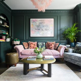 a dark green living room with panelled walls and a sugar pink velvet sofa, a large striking artwork on the wall