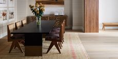 open plan dining room with large black dining table and rug, gallery wall, taupe wallpaper, and timber feature