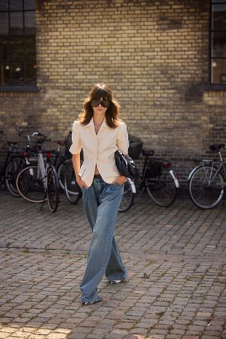 A woman at Fashion Week wearing a white fitted blazer and baggy blue jeans